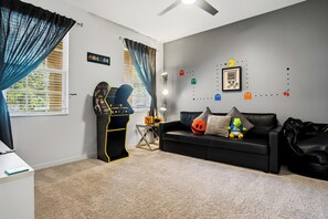 A living room with a black sofa, a gaming arcade machine, and a wall decorated with game-themed stickers.
