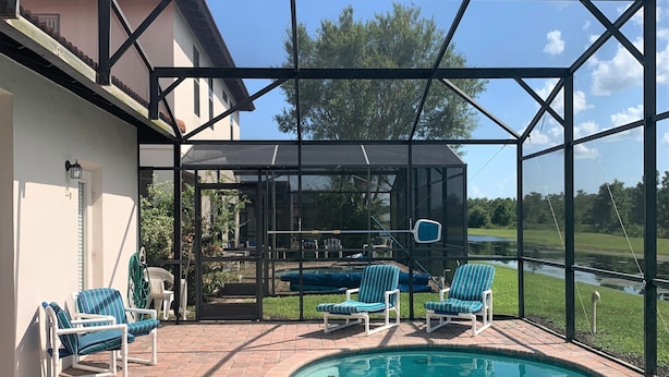 Ein überdachter Pool im Freien mit Liegestühlen, einem klaren blauen Himmel und einem Haus im Hintergrund.