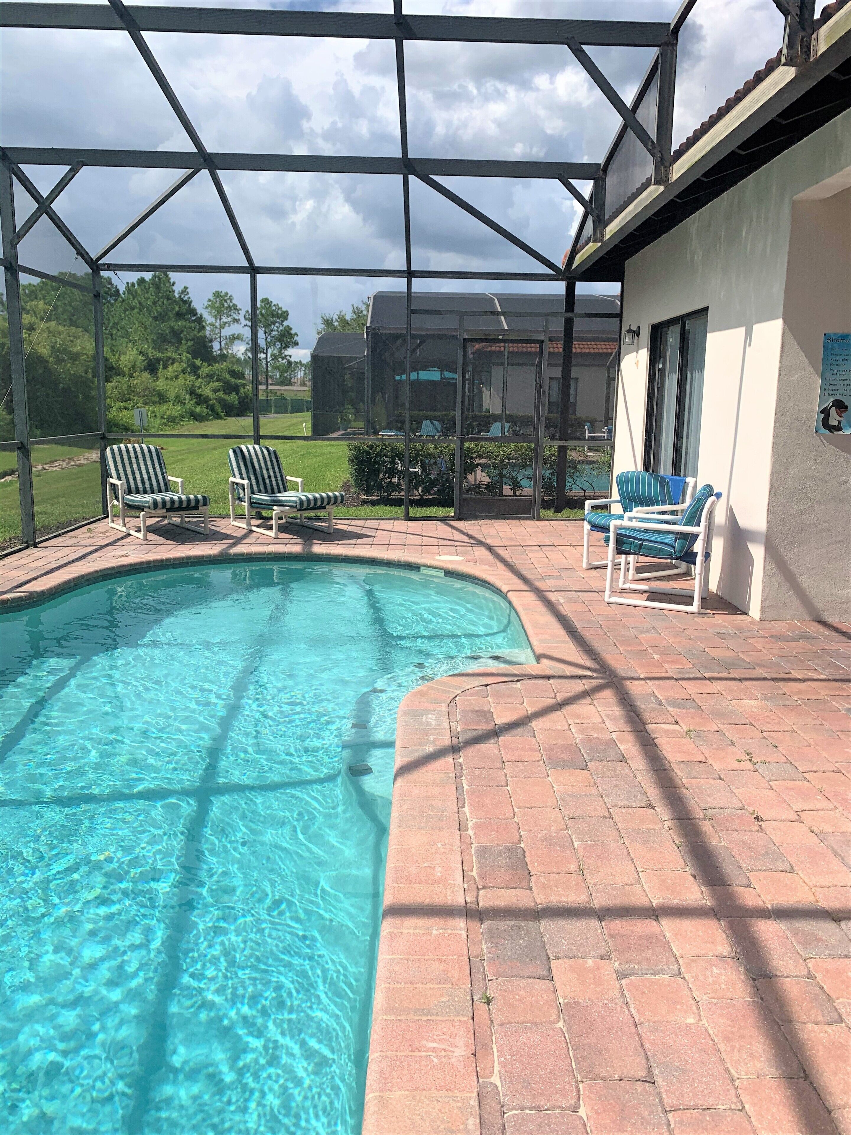A swimming pool with a covered patio area, including lounge chairs and a brick walkway.
