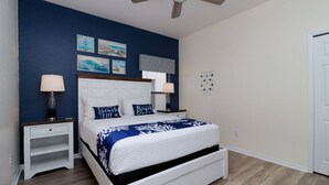 Ein Schlafzimmer mit einem Bett, zwei Nachttischen, einem Deckenventilator und Wandbildern.