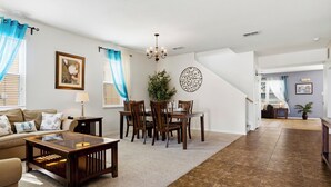 A living room with a sofa, coffee table, dining table, and chairs. There is a staircase leading to another level.