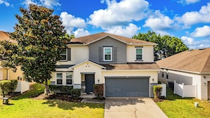 A two-story house with a garage, a front yard, and a tree.