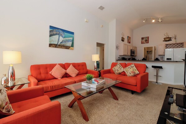 A living room with a glass coffee table, two red sofas, and a kitchen in the background. - Dreamville 4 Bedrooms (Davenport)