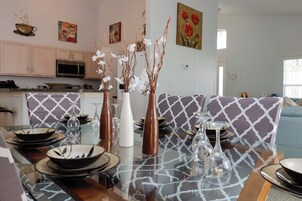 Uma sala de jantar com mesa de vidro posta para quatro pessoas, rodeada por cadeiras estampadas.