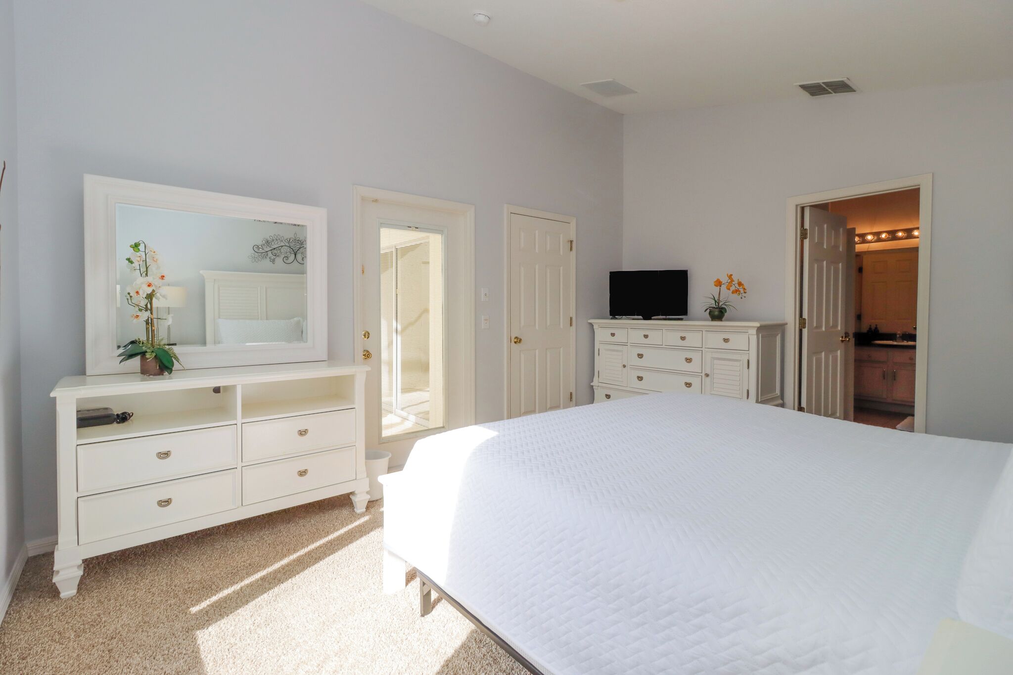 A bedroom with a large bed, a dresser with drawers, a television, and a door leading to another room.