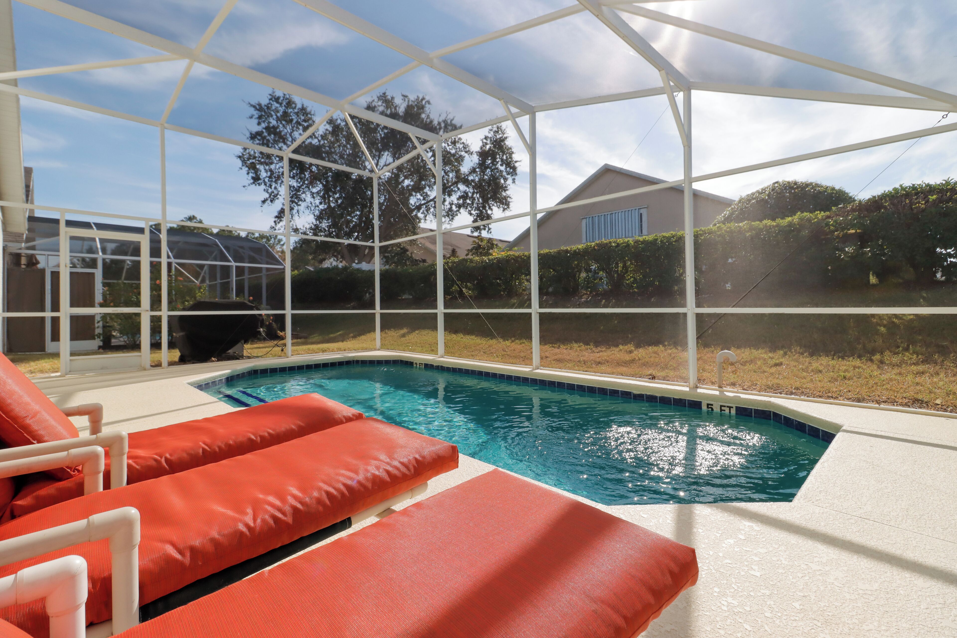 A pool area with red lounge chairs and a glass enclosure.