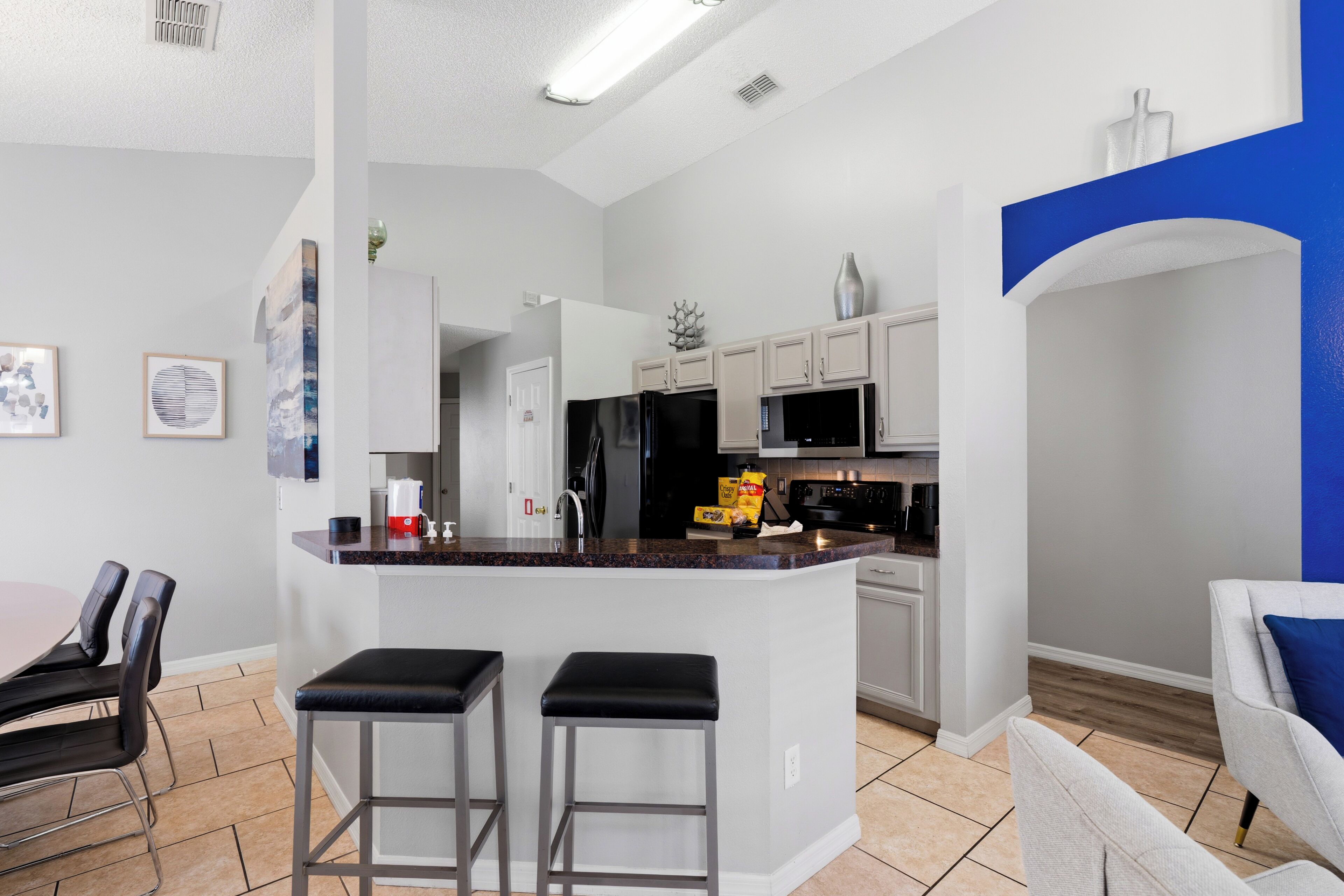 Een moderne keuken met een centraal eiland, barstoelen, een eethoek met stoelen en een blauwe accentmuur.
