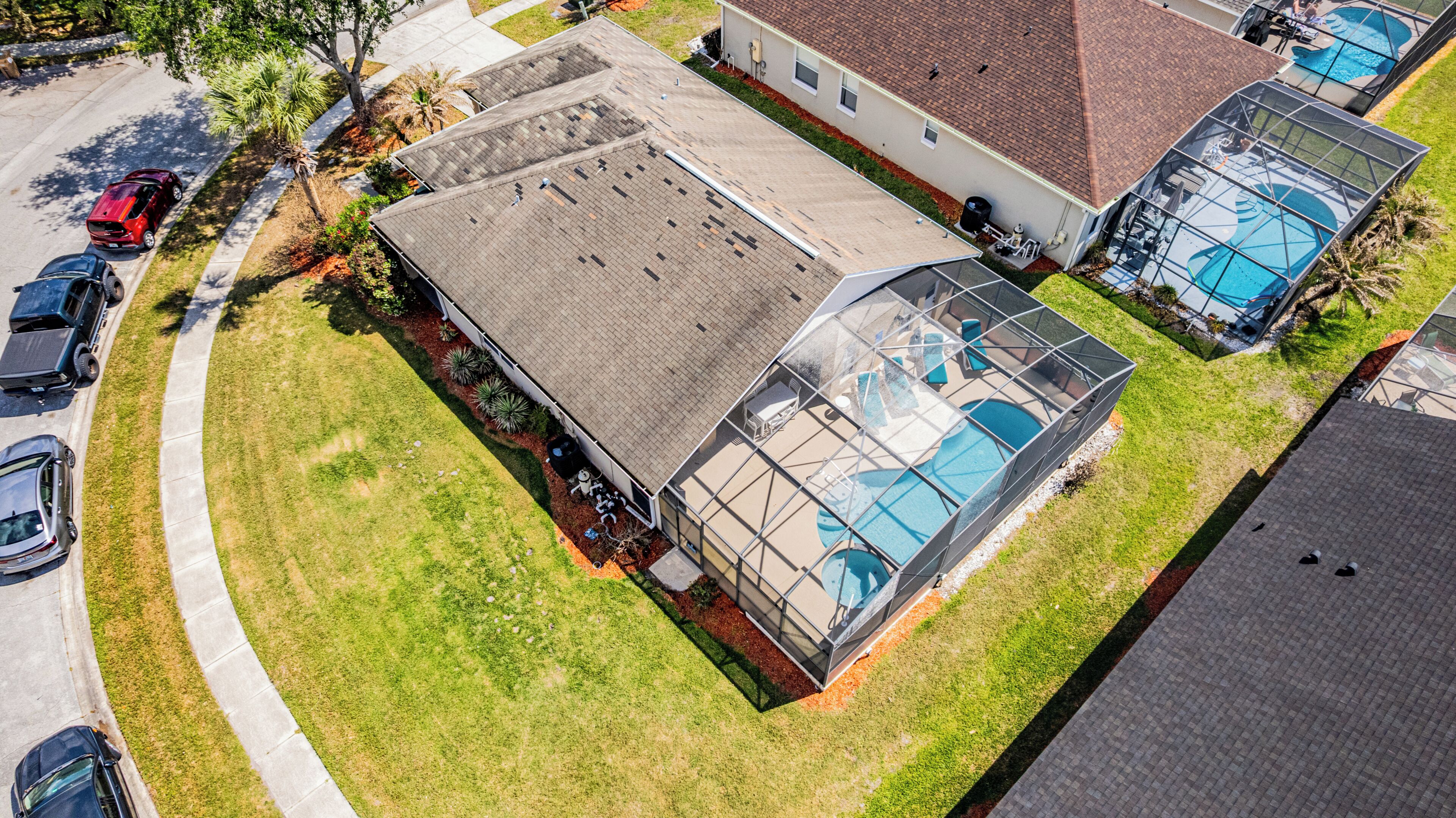 An aerial view of a residential property with a large glass-enclosed swimming pool, a covered patio area, and a spacious roof.