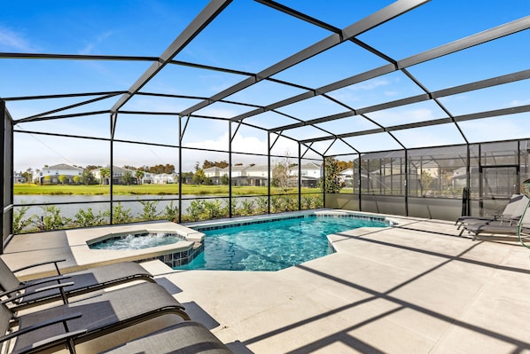 Una piscina exterior techada con sillones de descanso y un jacuzzi, rodeada por una estructura de metal y paneles de vidrio.