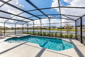 Une piscine dotée d’une structure en verre, un jacuzzi et une vue sur un lac et des maisons au loin.