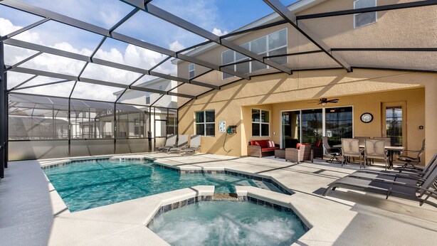 Une piscine entourée de parois en verre, avec un espace extérieur aménagé pour s’asseoir et une terrasse couverte.