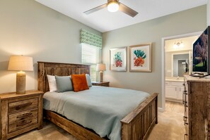 Une chambre à coucher avec un lit en bois, deux tables de chevet avec des lampes, un ventilateur de plafond et des œuvres d’art accrochées aux murs.