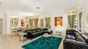 Una sala de estar moderna con un sofá de cuero negro, un tapete color turquesa y un comedor con mesa y sillas.