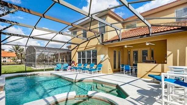 Un área de piscina con cerramiento de vidrio, sillas de descanso azules y un patio cubierto con mesas y sillas.