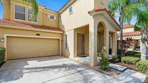 Una casa de dos pisos con fachada color beige, un garaje y un porche cubierto con columnas.