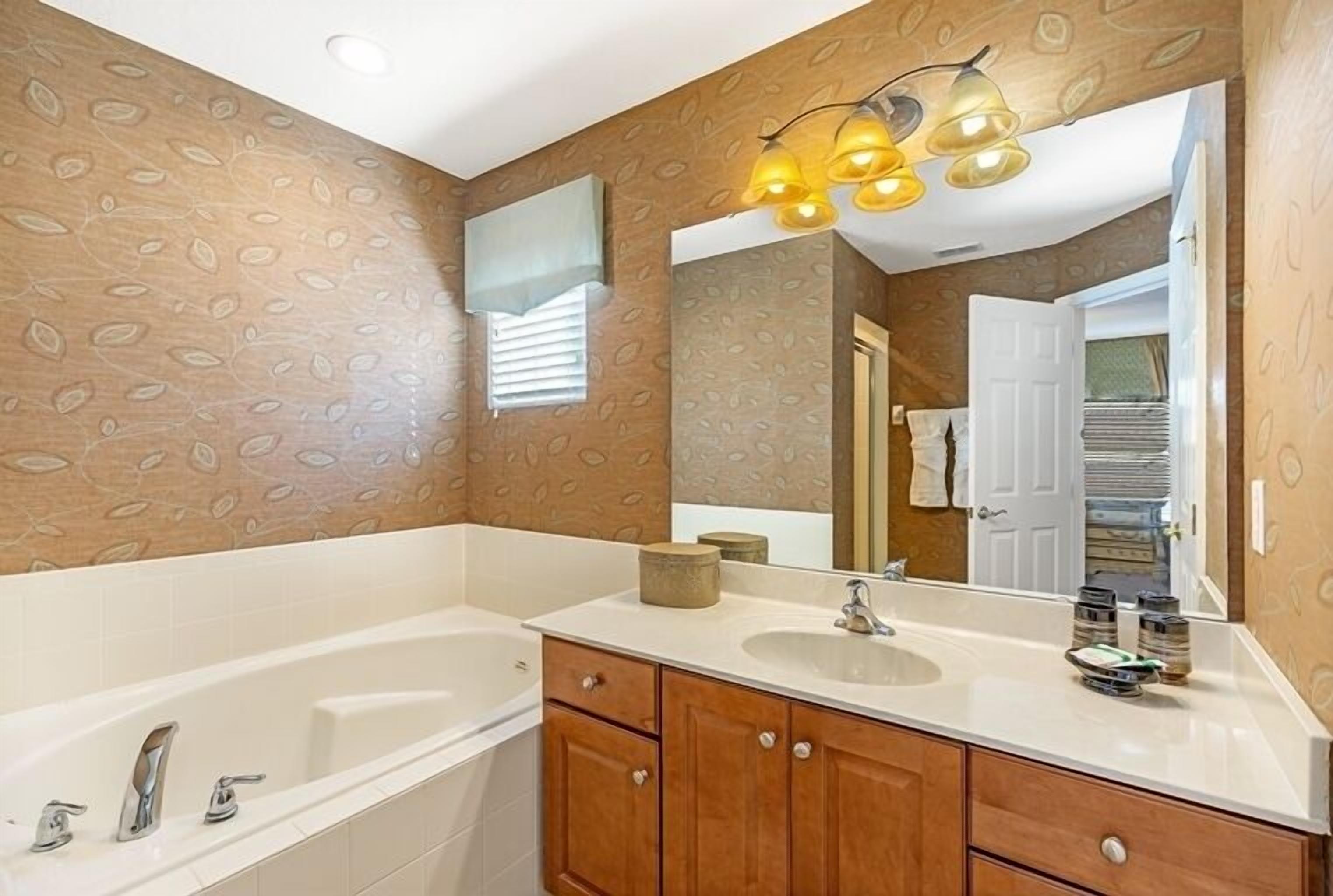 Une salle de bain avec une baignoire, un meuble-lavabo avec un miroir et un papier peint à motifs.