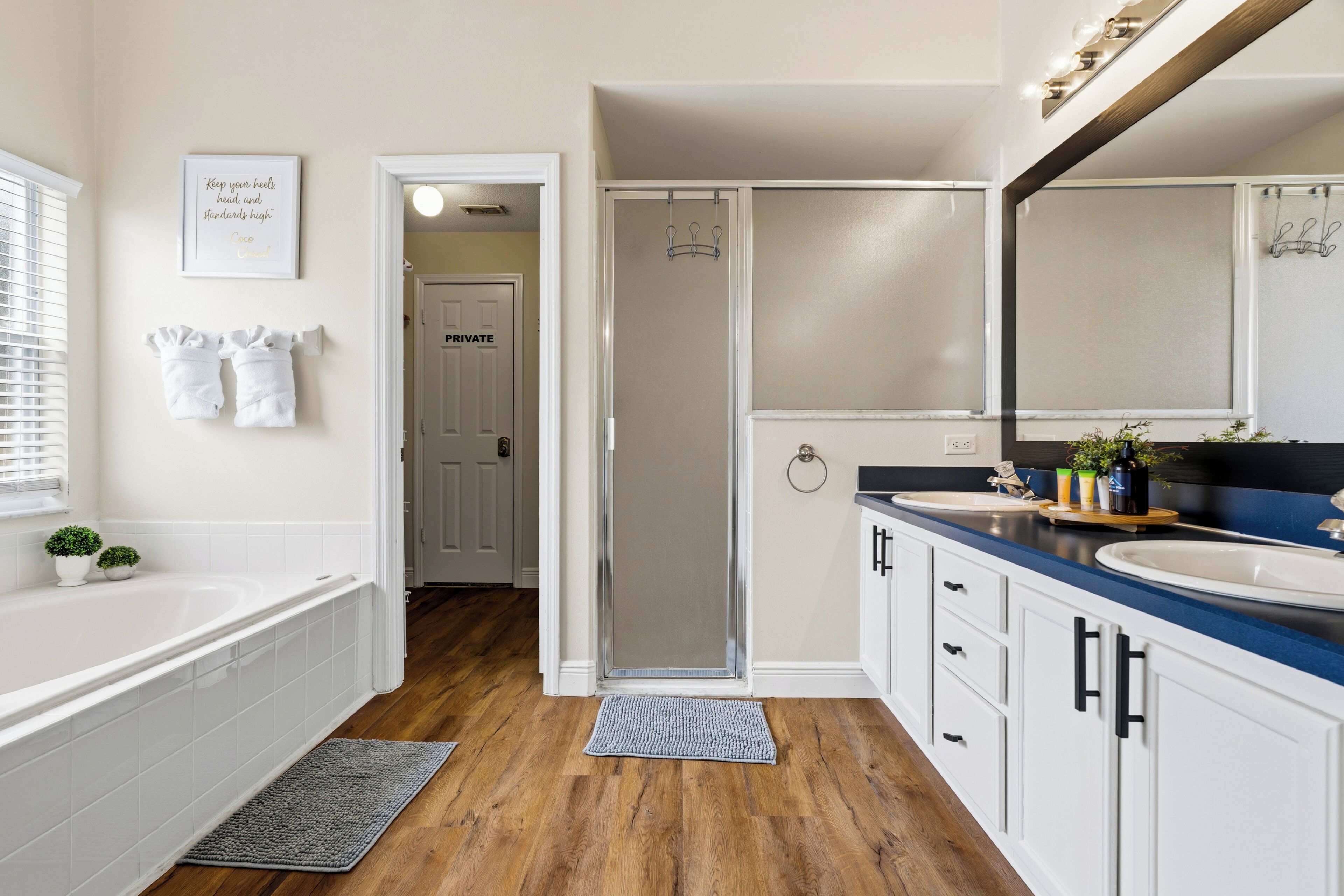 A modern bathroom with a bathtub, two sinks, a shower, and a vanity with a mirror.