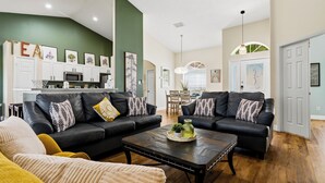 A living room with two black leather sofas, a coffee table, and a kitchen in the background. - Sapphire Sky Villa 4 Bedrooms (Clermont)