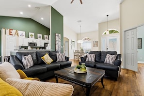 A living room with two black leather sofas, a coffee table, and a kitchen in the background. - Sapphire Sky Villa 4 Bedrooms (Clermont)