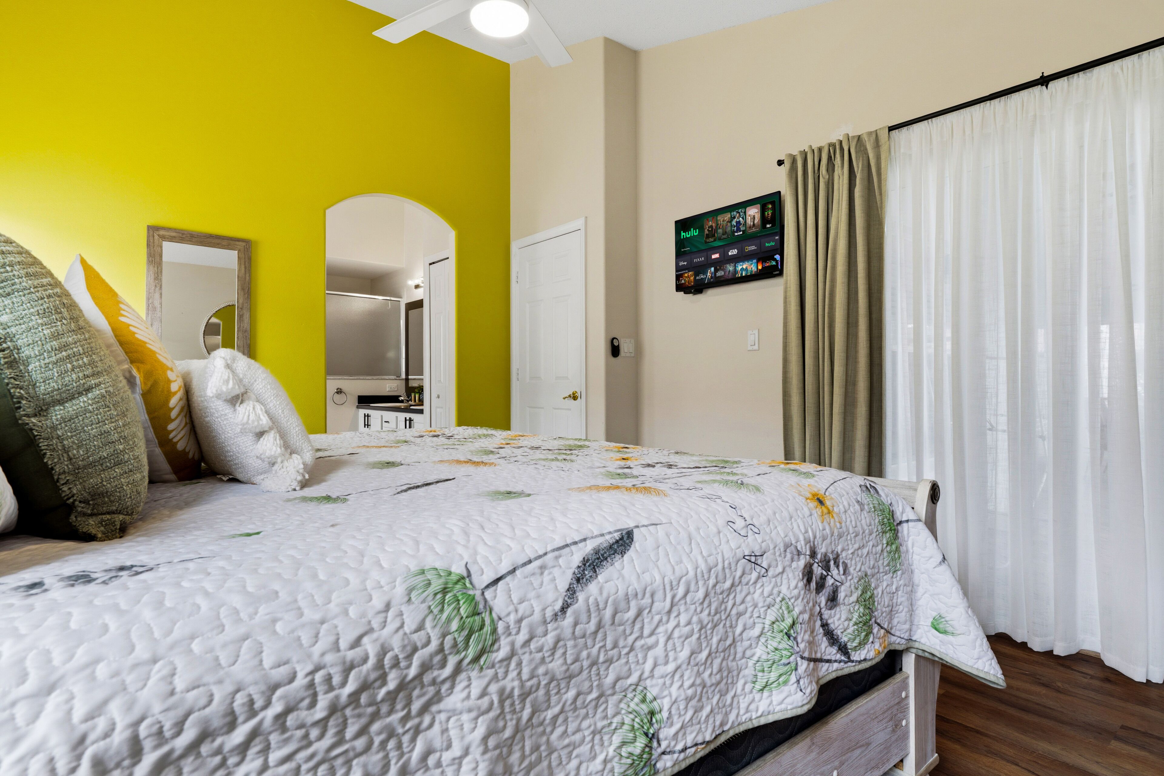 Une chambre à coucher avec un lit, un miroir, une porte et un téléviseur fixé au mur.