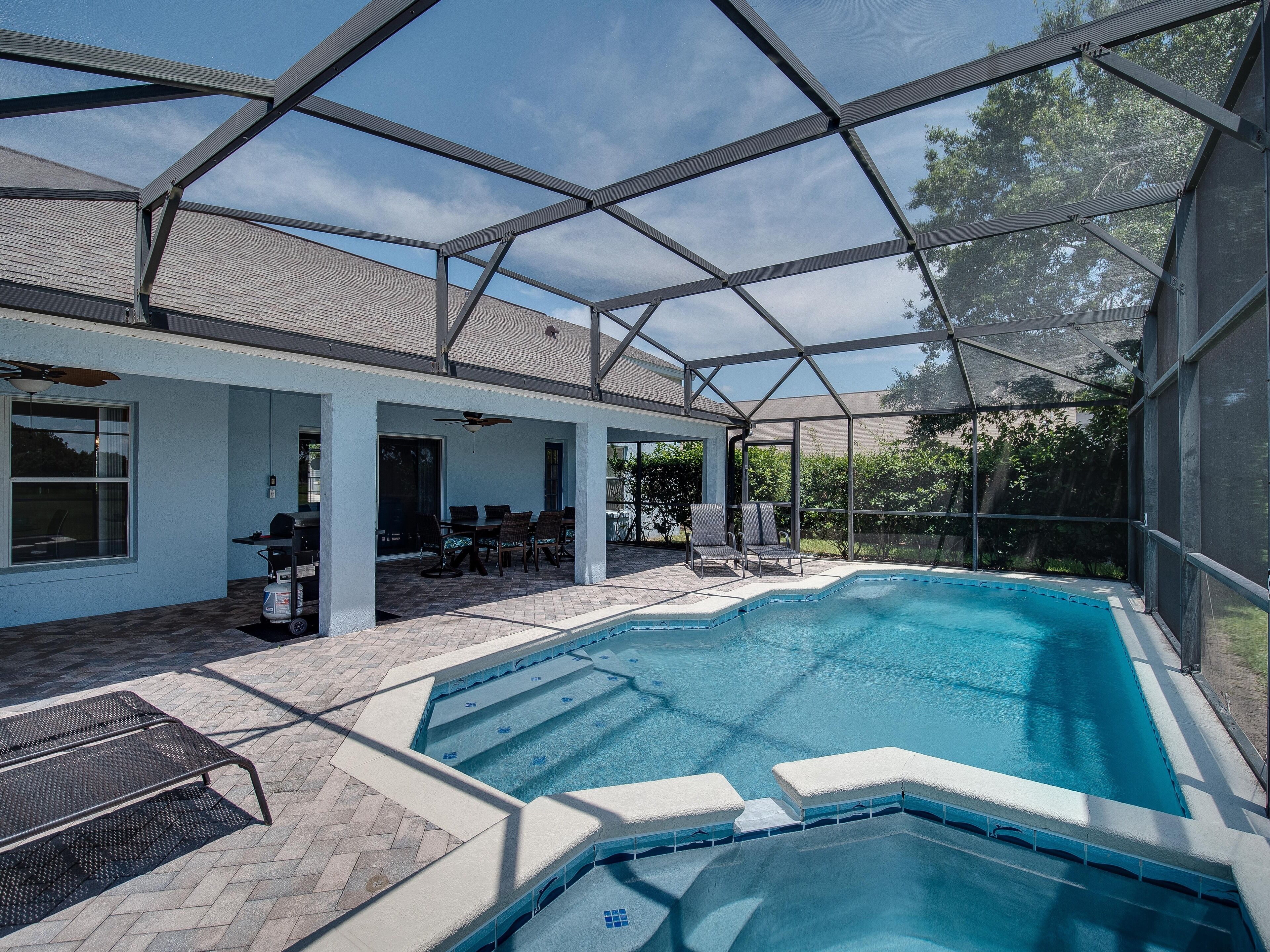 An indoor swimming pool with a glass ceiling, surrounded by a patio area with chairs and a table.
