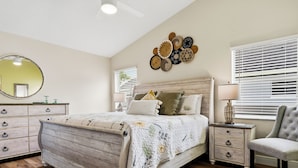 Une chambre à coucher avec un lit en bois, une table de chevet, une chaise, une commode, un miroir et des éléments de décoration murale.