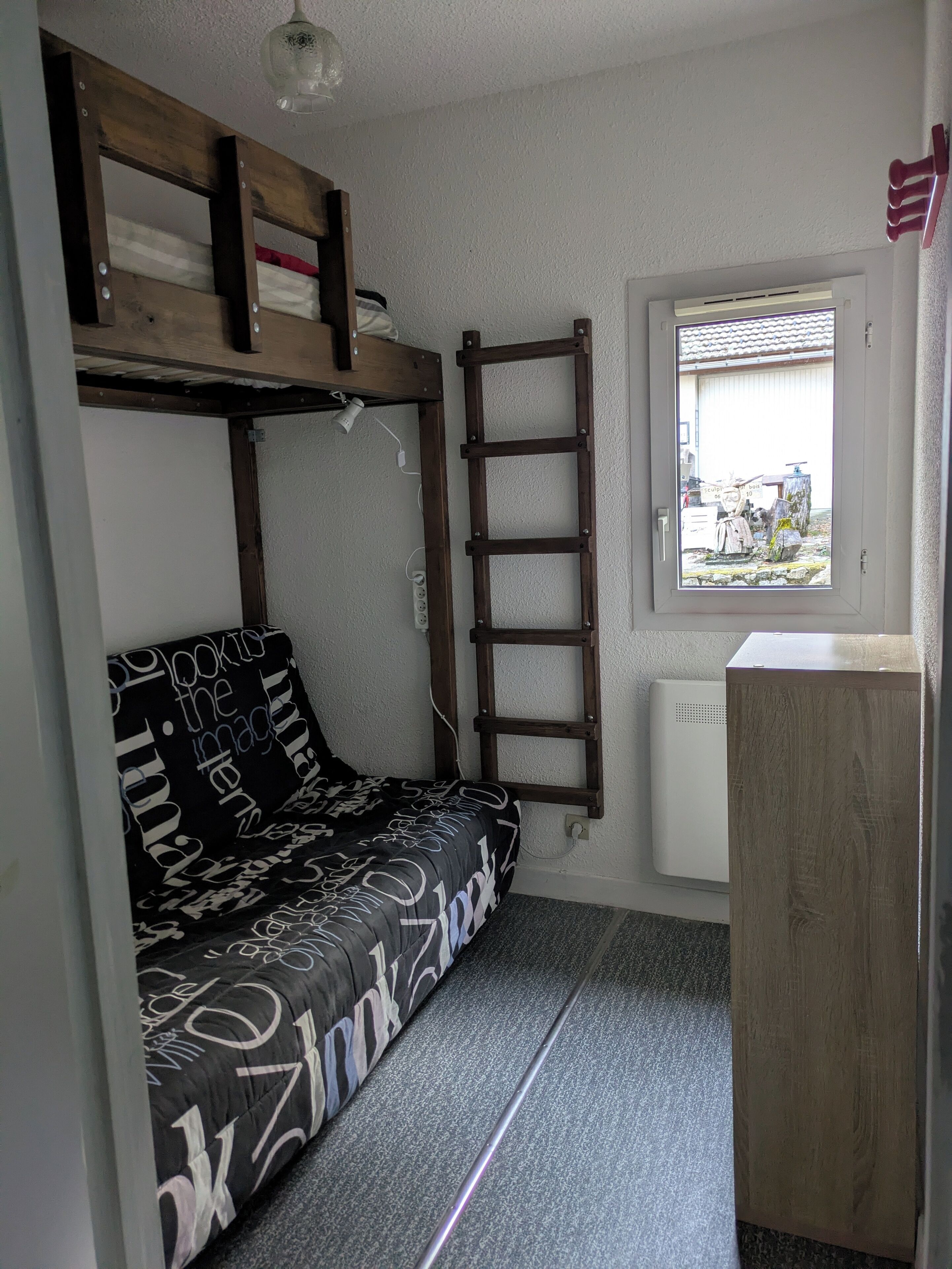Habitación pequeña con literas, una escalera, un escritorio y ventana con vistas al exterior.