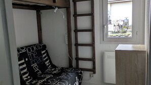 Habitación pequeña con literas, una escalera, un escritorio y ventana con vistas al exterior.