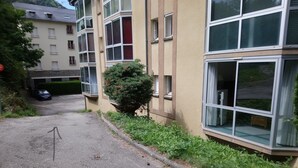 Una calle estrecha que conduce a un edificio con grandes ventanales y una zona de estacionamiento señalizada.