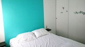 Un dormitorio con una cama, una pared verde azulado, una puerta blanca y una mesita de noche pequeña con una lámpara.