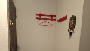 Una habitación pequeña y poco iluminada con una puerta, un perchero con ganchos, un banco pequeño y un gancho para abrigos en la pared.