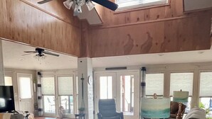 Amplia sala de estar con una mesa de comedor de madera, sillas, un sofá y una mesa de centro. Se observan ventanas grandes que dejan entrar luz natural, y un ventilador de techo.