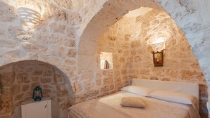 A stone-walled bedroom with a bed, a nightstand, and a lantern.