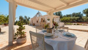 An outdoor dining area with a white table set for two, wicker chairs, and a potted plant.