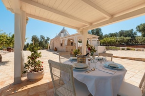 An outdoor dining area with a white table set for two, wicker chairs, and a potted plant.