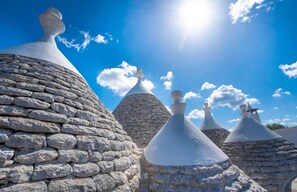 A row of stone buildings with conical roofs under a clear blue sky.