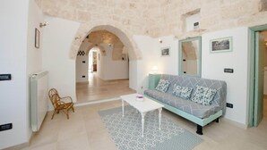 A living room with a stone ceiling, a sofa with patterned cushions, a white coffee table, and a wicker chair. - Trullo Paleo (Ceglie Messapica)