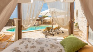 Quarto com vista para a piscina, com cama e colcha temática do mar, almofada verde e um dossel.