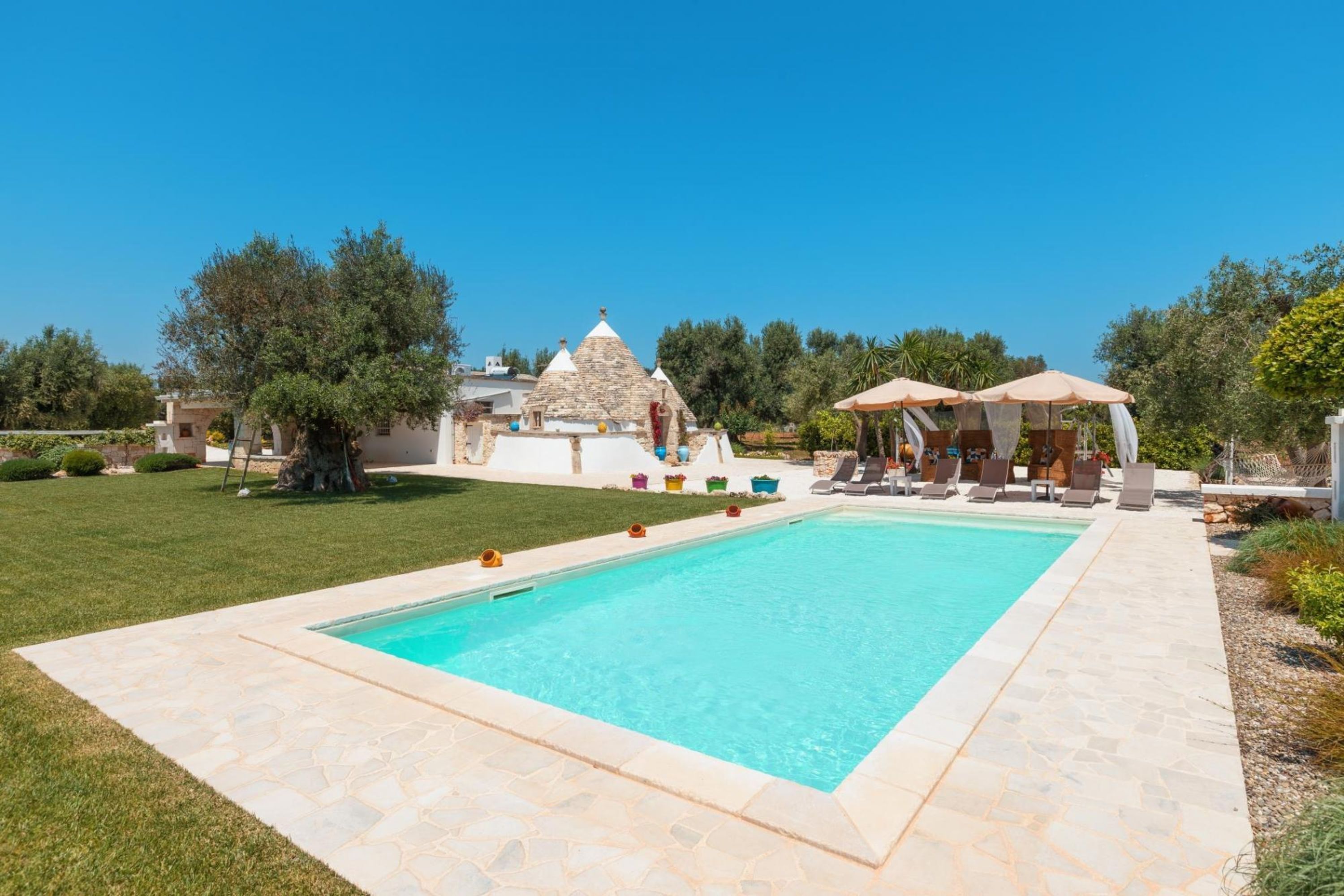 A swimming pool with lounge chairs and umbrellas, surrounded by a stone patio and greenery.