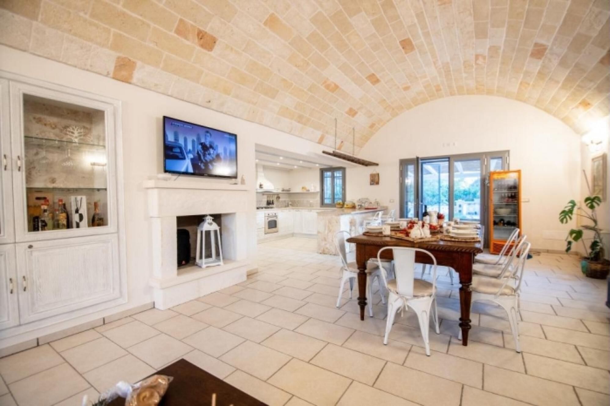 Amplia sala de estar con chimenea, una mesa de comedor con sillas, una cocina al fondo y un televisor montado en la pared.