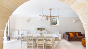 Une pièce spacieuse avec une table et des chaises de salle à manger blanches, un canapé marron et une fenêtre donnant sur des arbres.
