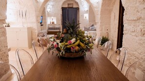 Et rustikt spiseområde med et træbord, klare stole og en frugt- og blomsterdekoration i midten.