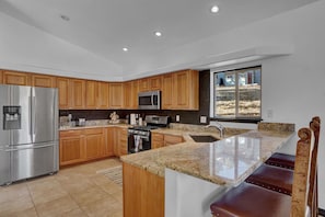 A modern kitchen with wooden cabinets, stainless steel appliances, a granite countertop, and a large window offering a view of the outdoors.