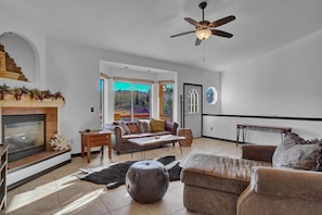A spacious living room with a fireplace, a sofa set, a coffee table, and a ceiling fan.