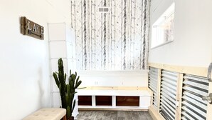 Um quarto pequeno e bem iluminado, com um banco, uma planta em vaso e uma placa na parede.