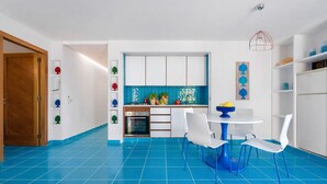 Una cocina moderna con armarios blancos, piso de azulejos azules y un comedor con sillas blancas y una mesa azul.