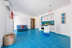 Une cuisine moderne avec des meubles blancs, un sol carrelé bleu et un coin repas avec des chaises blanches.