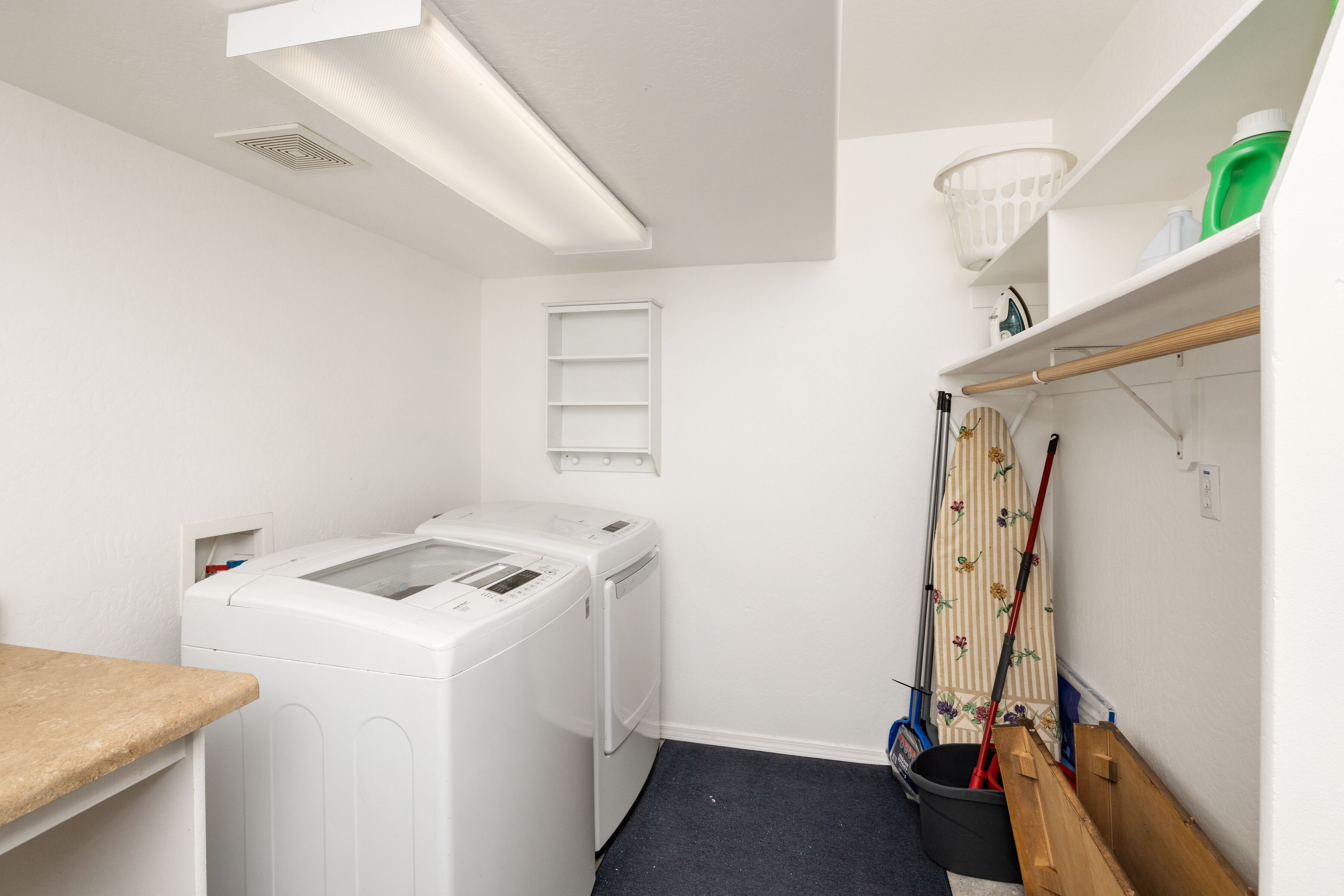 A laundry room with a washing machine, a drying rack, a broom, and a bucket.