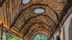 A covered outdoor area with wooden flooring and a thatched roof, featuring a seating area and a view of the surrounding greenery. - Alito Tulum Hotel (Tulum)