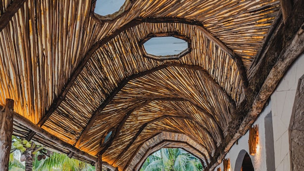 Un espacio al aire libre cubierto con suelo de madera y techo de paja, que incluye una zona de estar y vistas al entorno verde.